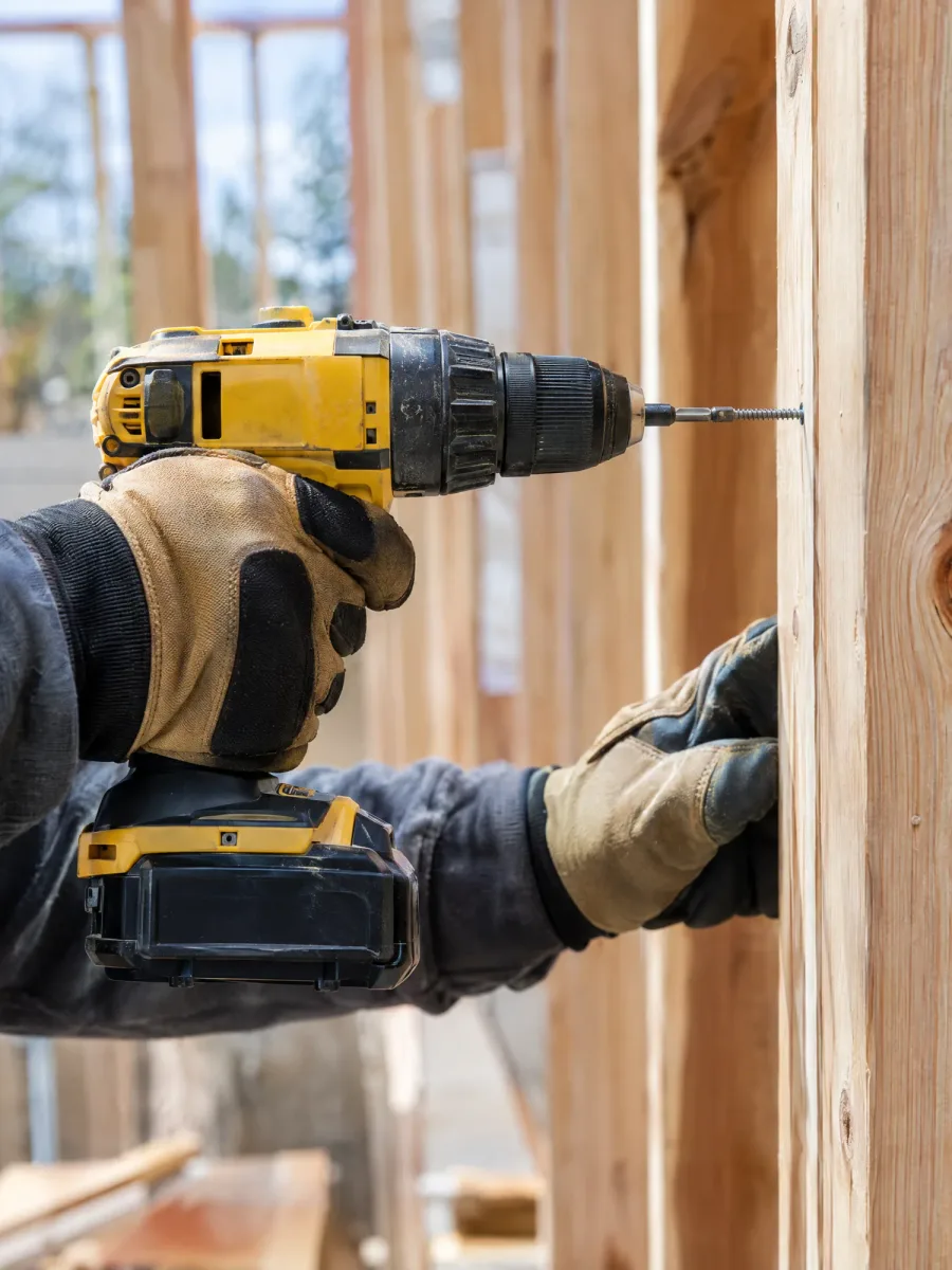 Gloved hands driving a screw into a timber stud with a cordless drill